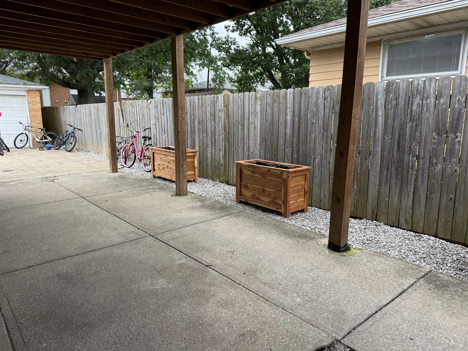 Wide view of delivered cedar planters beside the fence beneath the covered patio.
