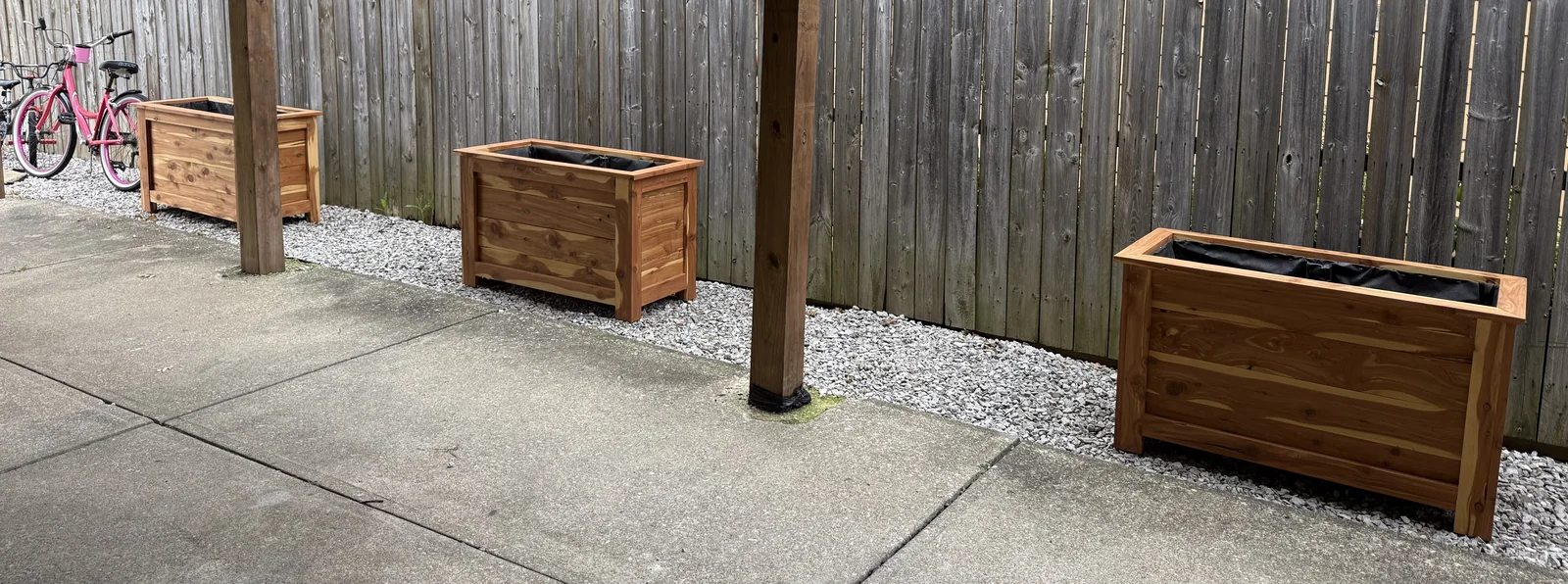 Three delivered cedar planters arranged along the fence beside a concrete patio.